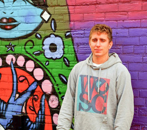 Dan Metcalfe, local artist of many talents, stands beside the mural he and another artist painted on the wall of Mrs. Tiggy Winkle’s. Photo: David Casey
